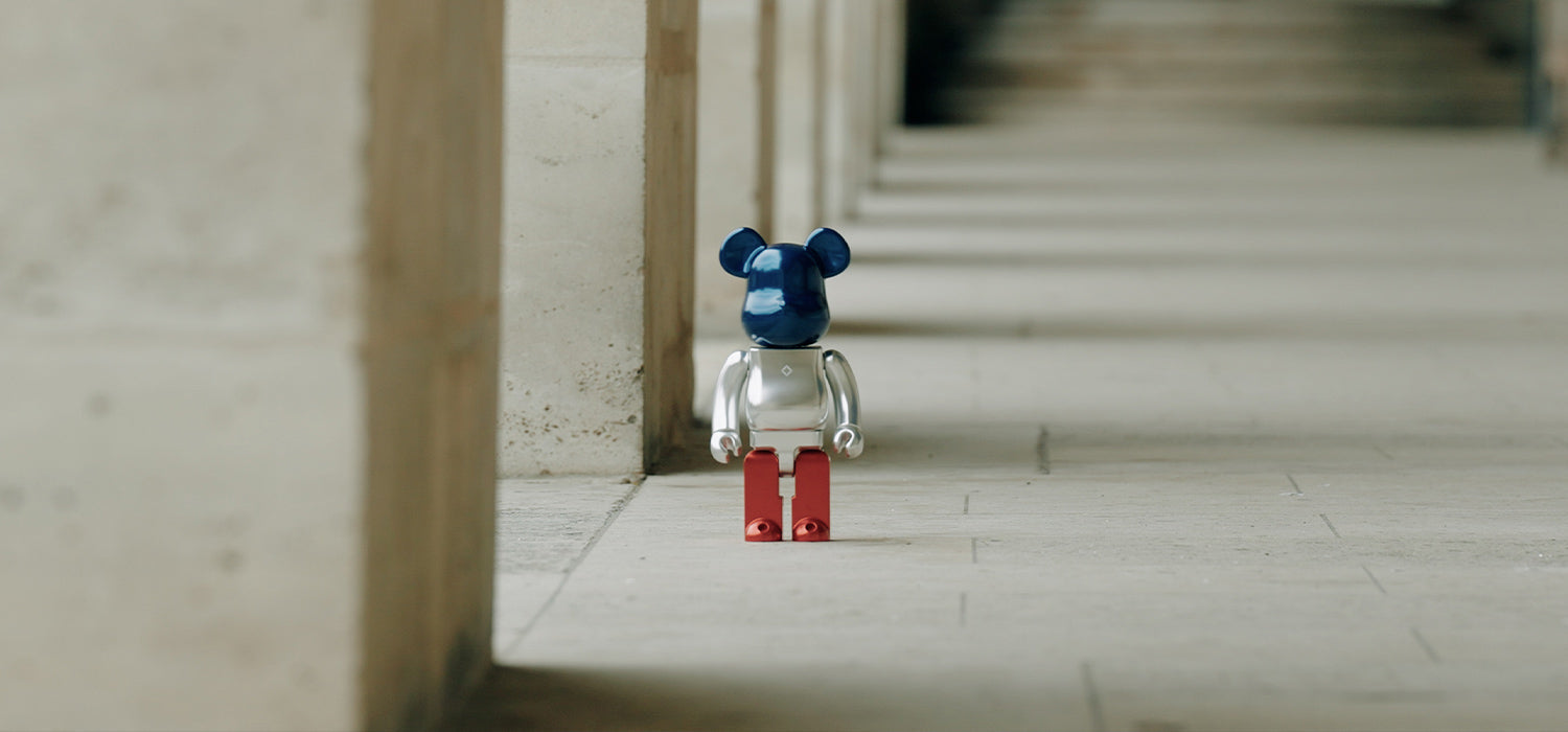 A metallic bear figure with a dark blue head, silver body, and red legs standing on a concrete floor
