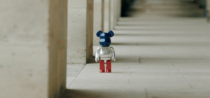 A metallic bear figure with a dark blue head, silver body, and red legs standing on a concrete floor