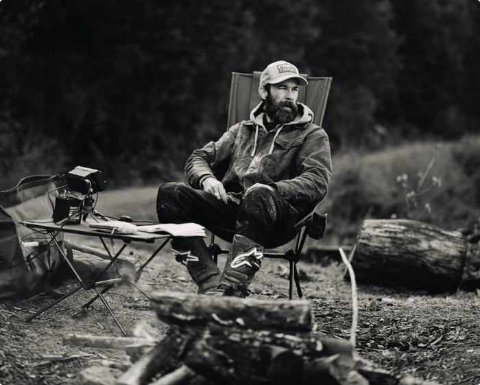 A bearded man sitting in a Helinox high-back camp chair by a campfire