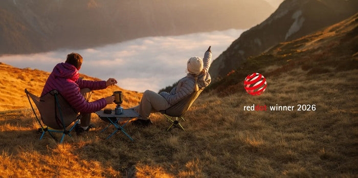 Two people sitting on camping chairs overlooking a mountain landscape.