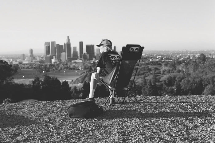 A man sitting in a Helinox x Obey high-back camp chair overlooking the Los Angeles city skyline