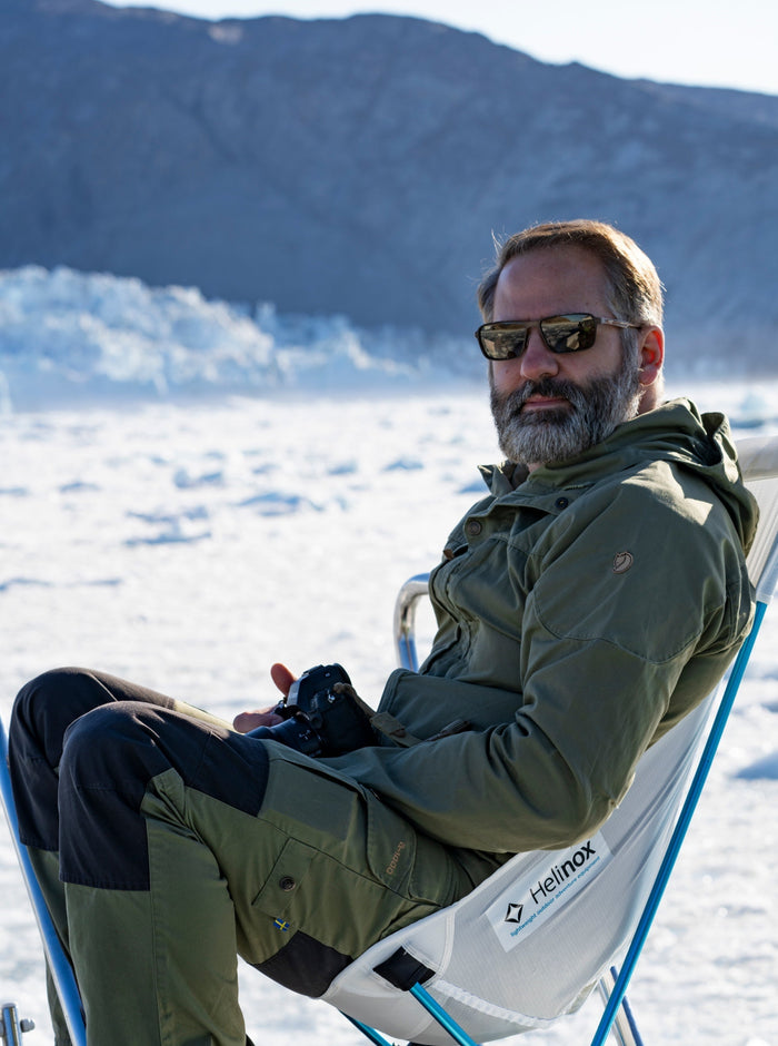 A man sitting on a Helinox chair surrounded by snow and mountains