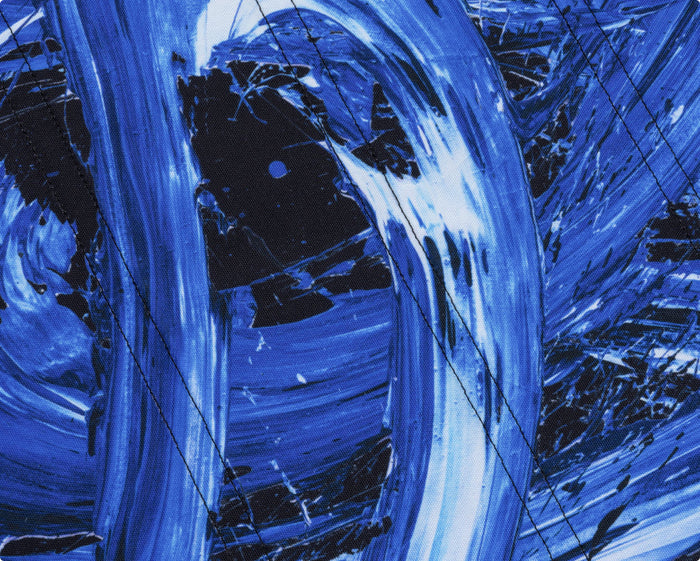 Close-up of fabric featuring an abstract blue and black paint brushstroke pattern with black stitching